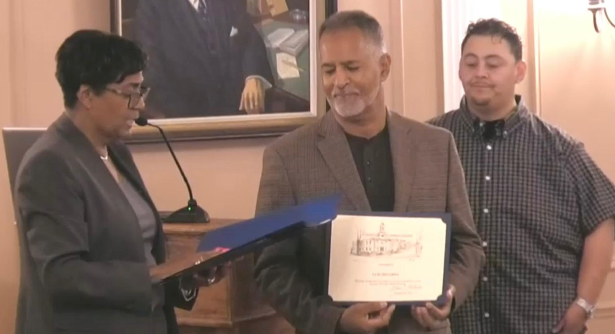 Mayor Vivian McKenzie reading from a proclamation. Holding certificate is Luis Segarra and Roy Escobar behind him. 