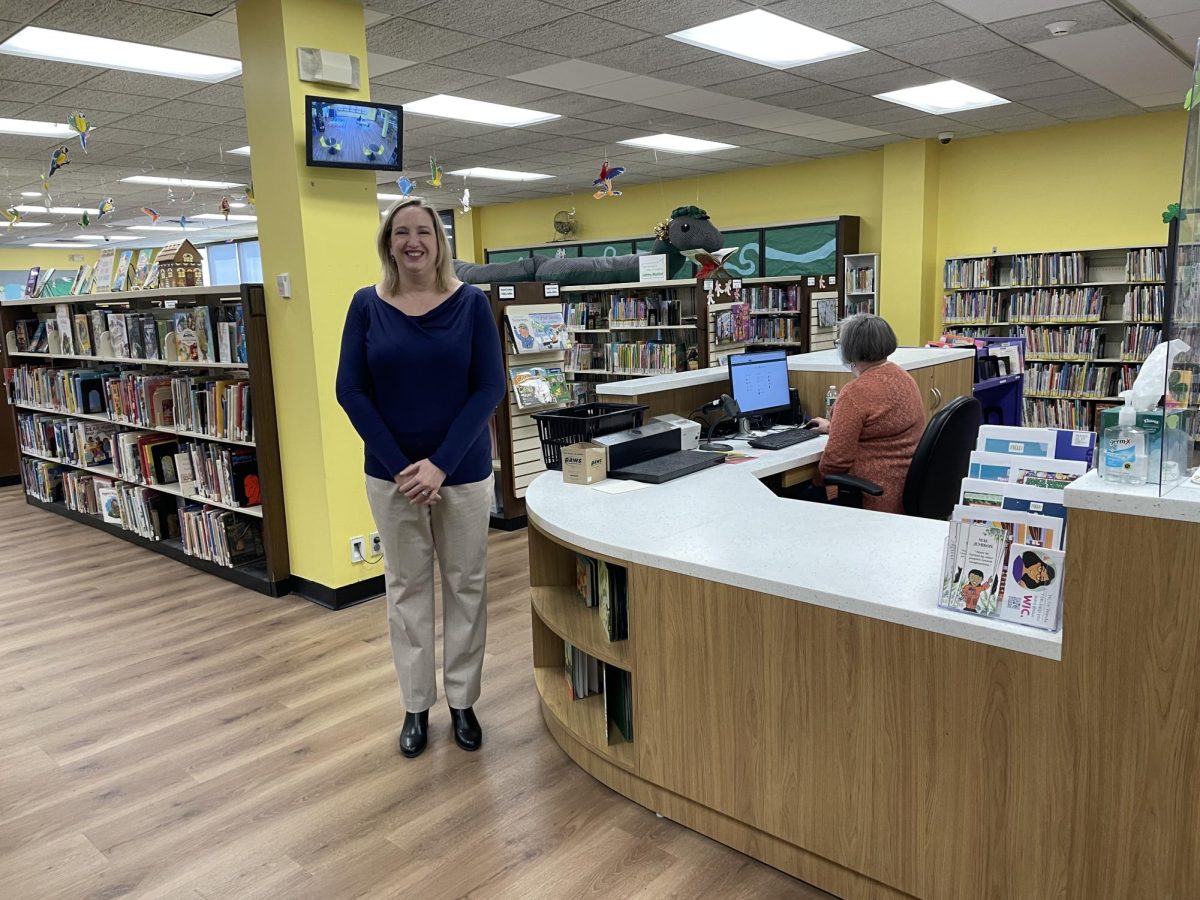 Outgoing Library Director Jennifer Brown at the revamped children’s circulation desk. New flooring, paint, and wiring are among her accomplishments.  (Photo by Regina Clarkin) 


