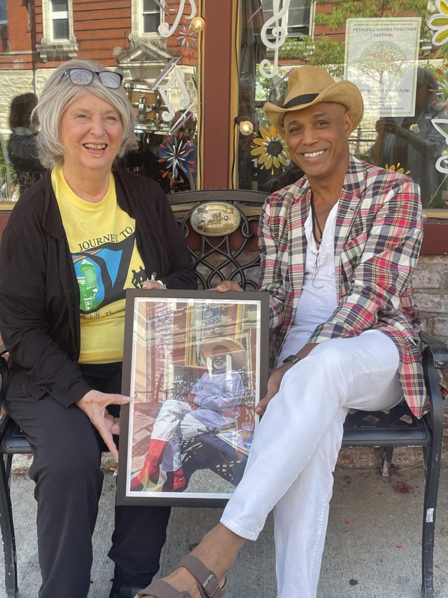 Sitting on the Terry Vonhightower bench that features his belt buckle is Scarlett Antonia and Wildred Morel. They are holding a photo of Vonghightower that is in the window of the Bean Runner Cafe.  