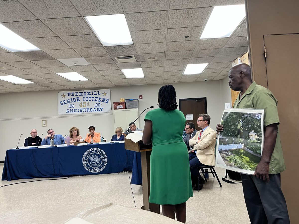 Regina Brons stands at the podium beside husband Richaro who holds a photo showing  a house that is in the backyard of the proposed microbusiness at 710 Washington Street. The site would only have cultivation and no retail. 